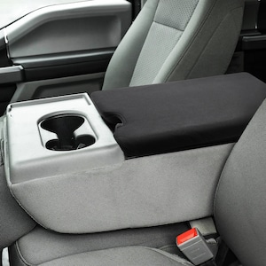 May include: Black center console armrest cover for a car. The cover is made of a soft, black fabric and has a built-in cup holder.