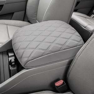 May include: A light gray car center console armrest cover featuring a diamond-stitched quilted pattern. The rectangular cover is fitted over the vehicle's center console lid, matching the surrounding gray interior upholstery and seating.