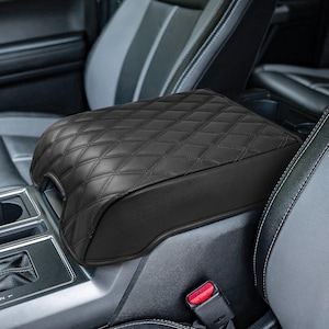 May include: Black quilted leather center console armrest cover for a car. The cover has a diamond pattern and is designed to protect the armrest from wear and tear.