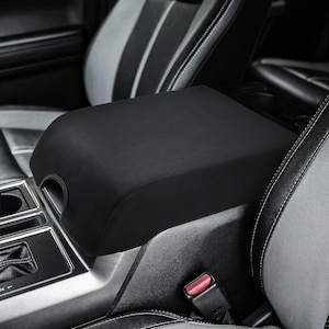 May include: Black car seat armrest cover. The cover is made of a soft, black fabric and fits snugly over the armrest. It is designed to protect the armrest from wear and tear.