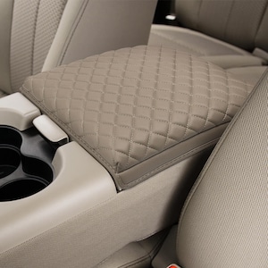 May include: A tan, quilted leather car armrest cover. The cover is diamond-stitched and fits over the center console armrest. The cover is shown in a car interior with tan and beige seats and cup holders.