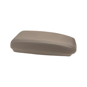 May include: A rectangular automotive center console armrest cover featuring a smooth, light taupe leather-like material with visible tonal stitching along the top edges. The piece has a contoured, padded design with a slightly tapered shape.