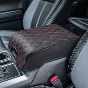 May include: Black leather center console armrest cover with red diamond stitching. The cover is designed to fit a car's center console.