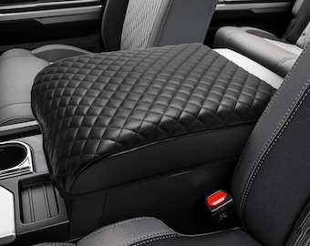 May include: Black quilted leather center console armrest cover for a car. The cover has a diamond pattern and is installed over the existing armrest.