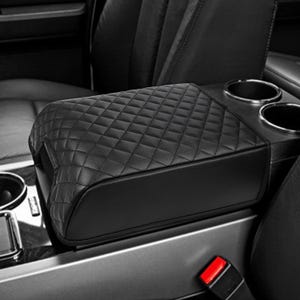 May include: Black quilted leather armrest cover for a car. The cover has a diamond pattern and is designed to fit over the existing armrest.