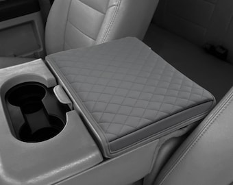 May include: Gray quilted car seat cover with a built-in cup holder. The cover is designed to fit over the center console armrest of a vehicle.