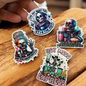 May include: A collection of four colorful stickers with skeleton-themed designs. One sticker reads "ON MY WAY TO STIR THE POT", another says "MIND YOUR OWN MOTHERHOOD", a third says "JUST WAITING FOR MY SOURDOUGH TO RISE", and the last one says "HOT MESS EXPRESS".