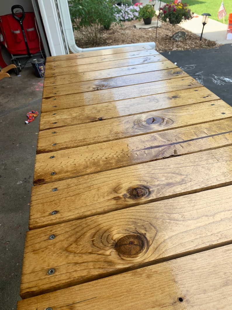Pu&ograve; includere: Primo piano di un piano da tavolo in legno con finitura naturale. Il piano del tavolo &egrave; composto da diverse assi di legno unite tra loro. Il legno ha una tonalit&agrave; calda color miele ed &egrave; rivestito da un sigillante trasparente. Il piano del tavolo &egrave; liscio e lucido, e la venatura del legno &egrave; visibile.