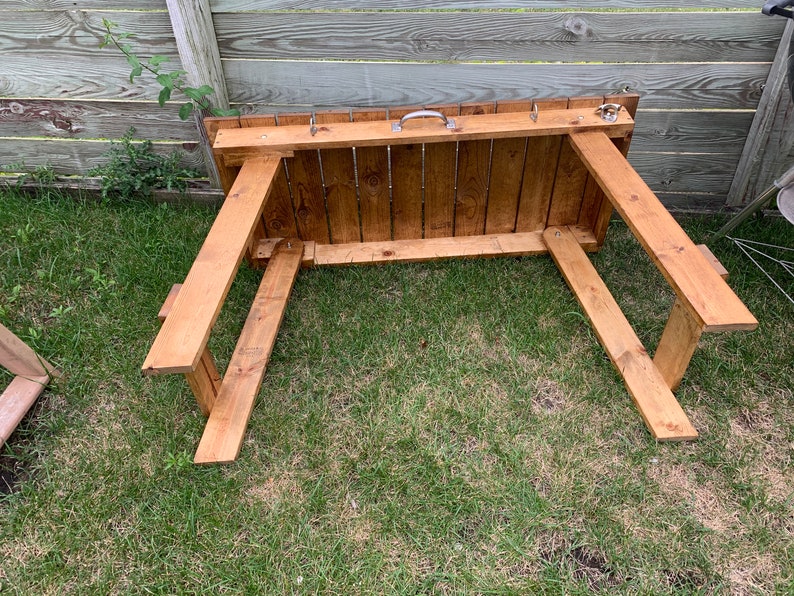 Pu&ograve; includere: Un tavolo in legno con una finitura in tinta marrone. Il tavolo ha un design semplice con un piano rettangolare e quattro gambe. Il tavolo &egrave; appoggiato su una superficie erbosa.