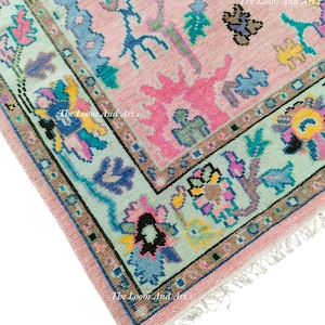May include: A pink rug with a light blue, green, and yellow floral pattern. The rug has a fringe border and the text "The Loom And Arts" is visible in the image.