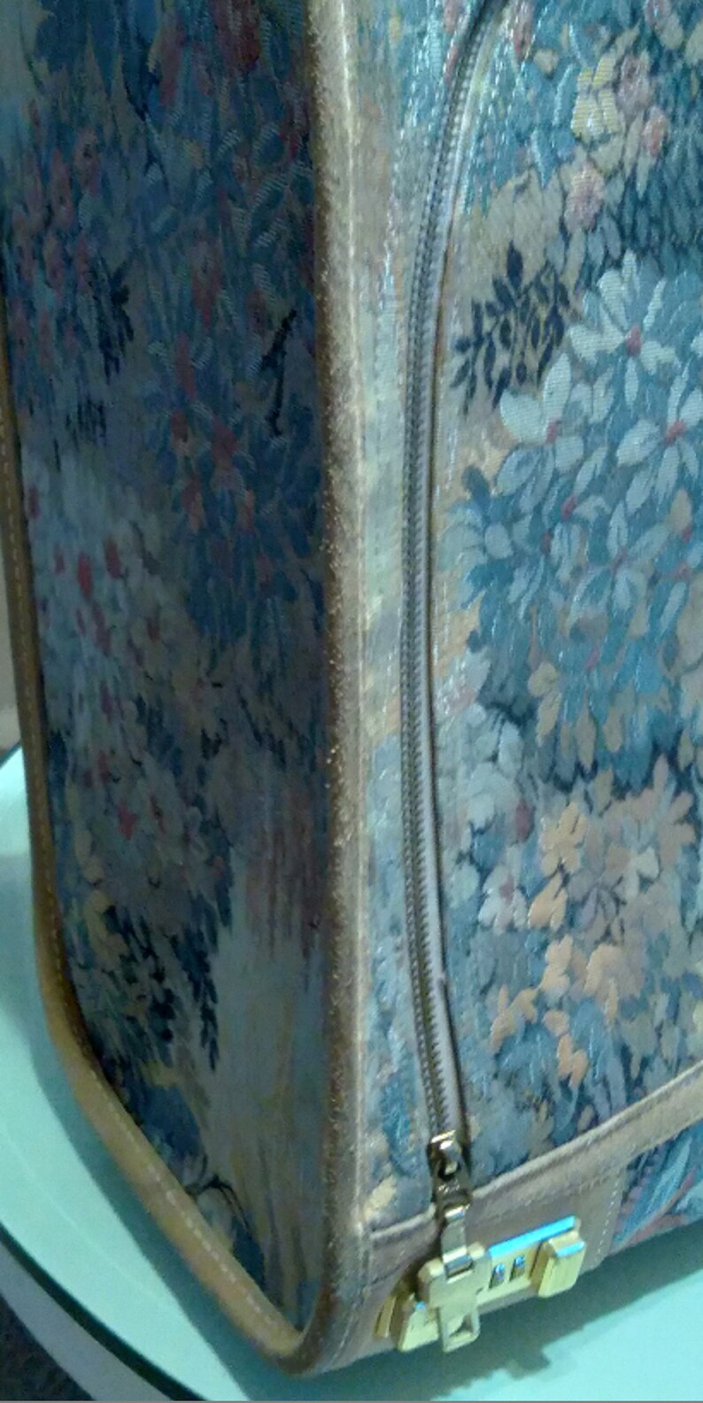 May include: A vintage floral patterned suitcase with a zipper closure and a gold metal latch. The suitcase is made of a soft, textured fabric.
