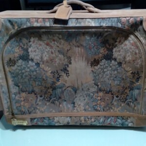May include: A vintage suitcase with a floral tapestry design. The suitcase is brown with a tan leather trim and a handle.