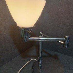 May include: A chrome desk lamp with a white frosted glass shade. The lamp has a flexible arm and a round base.