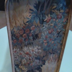May include: A beige vintage suitcase with a floral tapestry design. The tapestry features a variety of flowers, leaves, and trees in shades of blue, green, red, and white.