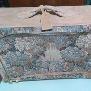 May include: A vintage floral tapestry suitcase with a tan leather trim and handle. The suitcase has a zipper closure and a luggage tag.