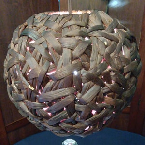 May include: A brown woven lampshade with a light shining through the gaps in the weave.