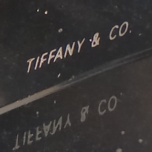 May include: Close-up of a black surface with the text "TIFFANY & CO." engraved in silver lettering.