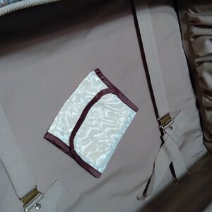 May include: The inside of a beige suitcase with a white and brown patterned fabric lining. A small white and brown pouch with a maroon trim is visible in the center of the image.
