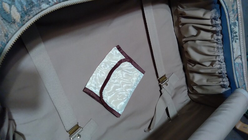 May include: The inside of a beige suitcase with a white and brown patterned fabric lining. A small white and brown pouch with a maroon trim is visible in the center of the image.