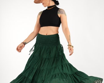 May include: A woman wearing a black crop top and a green tiered skirt with lace trim. She is wearing a brown hat and has her hair pulled back. The skirt is flowing in the wind.