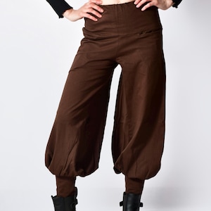 May include: Brown harem pants with a high waist and gathered ankles. The pants have a loose, flowing fit through the legs and are paired with black ankle boots. The model is wearing a black long-sleeved top.