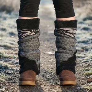 May include: A person wearing black leggings and brown boots with patterned leg warmers. The leg warmers have a geometric design in gray and black, with a zebra-striped pattern at the top.