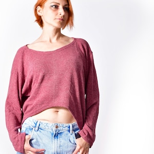 May include: A maroon long-sleeved top with a wide neckline and light blue denim jeans. The top is cropped, revealing the midriff. The jeans have a classic five-pocket design.