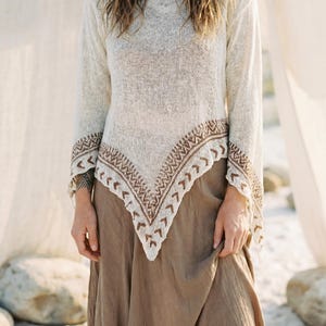 Könnte beinhalten: Cremefarbener Strickpullover mit langen Ärmeln und einem dekorativen braunen geometrischen Muster am Saum und an den Manschetten. Dazu ein langer, fließender brauner Rock, für einen Boho-Look.