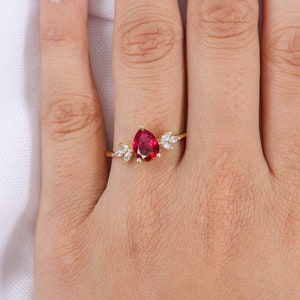 May include: A gold ring featuring a pear-shaped red gemstone and smaller white gemstones on the band.
