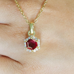 May include: A gold chain necklace with a red gemstone pendant surrounded by smaller clear gemstones.