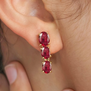 Peut inclure: Une paire de boucles d'oreilles en or avec trois pierres précieuses ovales rouges suspendues à chaque boucle d'oreille.