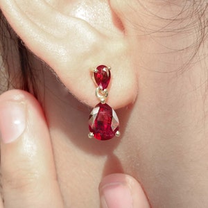 Puede incluir: Un par de pendientes de oro con piedras preciosas rojas en forma de lágrima.