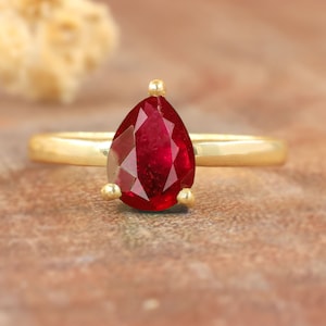 Peut inclure: Une bague en or sertie d'une pierre précieuse rubis de forme poire. La bague est simple et élégante, avec une bande lisse et une seule pierre précieuse proéminente.