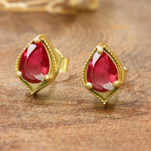 Peut inclure: Une paire de boucles d'oreilles en or avec des pierres précieuses rouges en forme de larme. Les boucles d'oreilles ont un design délicat et orné.