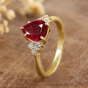 May include: A gold ring featuring a large pear-shaped ruby gemstone surrounded by smaller diamonds.