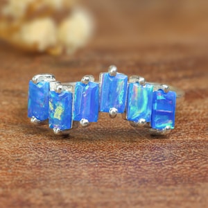 May include: A silver ring with a row of blue opal stones set in a curved shape.