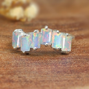 Könnte beinhalten: Ein silberner Ring mit einer Reihe von sechs schillernden Opal-Steinen, die in einer gebogenen, rechteckigen Form gefasst sind.