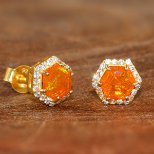 May include: A pair of gold earrings with a hexagonal orange opal gemstone surrounded by a halo of small clear cubic zirconia stones.