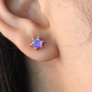 Peut inclure: Gros plan sur une oreille avec une petite boucle d'oreille en opale violette. La boucle d'oreille est sertie d'or.