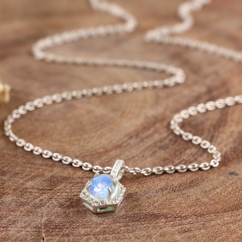 Pu&ograve; includere: Una collana con catena d'argento con un ciondolo esagonale che presenta una pietra di luna blu circondata da pietre pi&ugrave; piccole e trasparenti.