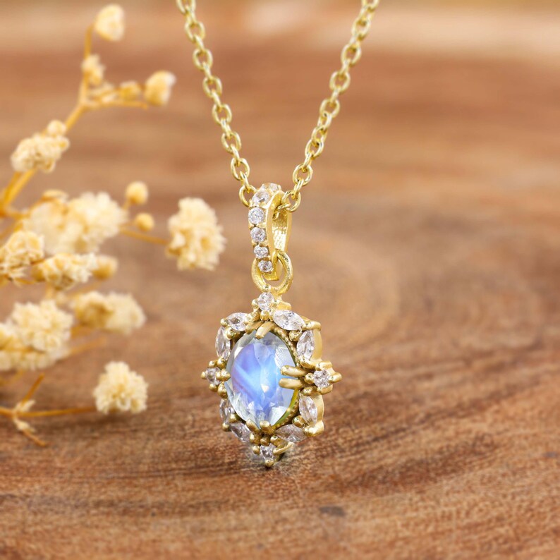 May include: A gold-colored necklace with a pendant featuring a blue gemstone. The pendant is surrounded by smaller, clear gemstones. The necklace is displayed on a wooden surface.
