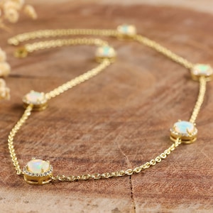 May include: A gold chain necklace with five oval-shaped opal stones set in a halo of smaller diamonds. The necklace is on a brown wooden surface.