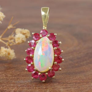 Könnte beinhalten: Ein birnenförmiger Opal-Anhänger in Gold mit einem Heiligenschein aus roten Rubinen.