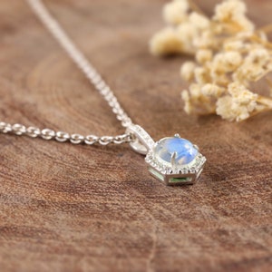 Pu&ograve; includere: Una collana d'argento con un ciondolo esagonale che presenta una pietra di luna blu circondata da pietre trasparenti pi&ugrave; piccole e accenti verdi.