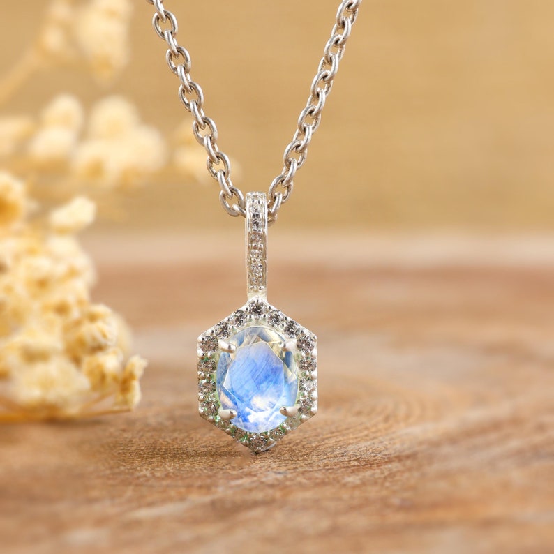 Pu&ograve; includere: Una collana d'argento con un ciondolo esagonale che presenta una pietra di luna blu circondata da pietre pi&ugrave; piccole e trasparenti.