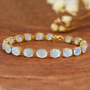 May include: A gold bracelet featuring oval-shaped opals. The opals display a play of color with iridescent hues of blue, pink, and green. The bracelet is set on a gold chain, creating a delicate and elegant piece of jewelry.