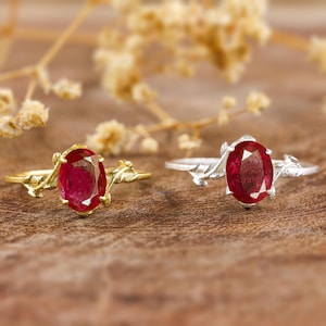 Puede incluir: Dos anillos con una piedra preciosa roja engastada en un diseño de hoja. Un anillo es de oro y el otro de plata.