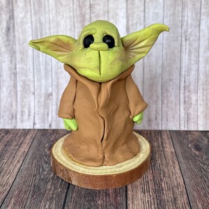 May include: A green and brown handmade figurine of a popular fictional character, standing on a wooden base.