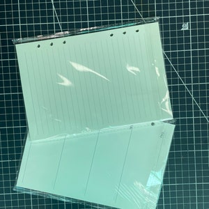 May include: A pack of two white lined paper refills for a planner or notebook. The paper is in a clear plastic sleeve and has holes punched along the top edge. The paper has the word "THU" printed on the bottom right corner.