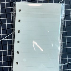 May include: A white, lined, paper refill for a 6-ring binder. The paper is packaged in a clear plastic sleeve.